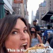 a woman is eating a sandwich on a city street and says this is for you baby .