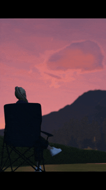 a person is sitting in a chair looking at a pink sky