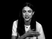 a woman with long hair is wearing a white t-shirt and waving her hand in a black and white photo .