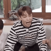 a man in a striped shirt is sitting on a couch with his mouth open and making a funny face .
