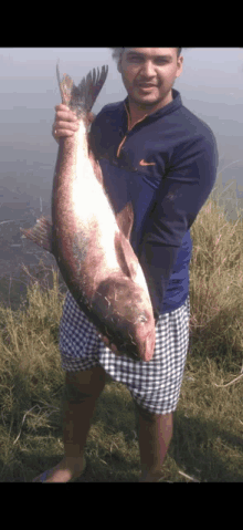 a man in a nike shirt holds a large fish in his hands