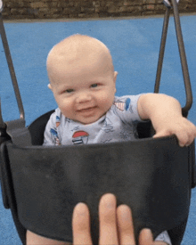 a baby wearing a sailboat shirt is sitting in a black swing