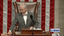 a man in a suit and bow tie sits in front of a microphone and a sign that says c-span