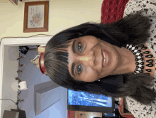 a woman wearing a headband and a necklace smiles in front of a picture on the wall that says " i love you "