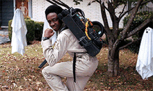 a man in a ghostbusters costume is kneeling down in front of a tree with ghosts in the background .