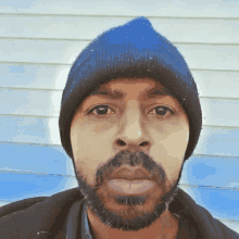 a man with a beard wearing a blue beanie looks at the camera