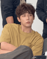 a young man in a yellow t-shirt is sitting down