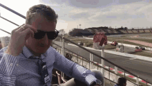 a man wearing sunglasses and a name tag that says ' ferrari ' on it sits in front of a race track