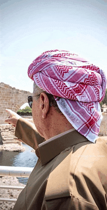 a man wearing a red and white head scarf points to a body of water