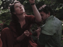 a man and a woman are sitting in the woods looking up at something