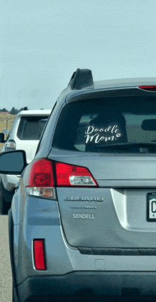 a silver subaru with a sticker on the back window that says " doodle mom "