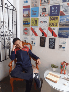 a young boy sits in a chair in front of a wall with signs on it including one that says born to fly