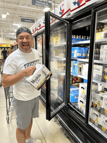 a man holding a box of modelo beer in front of a fridge