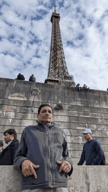 a man stands in front of the eiffel tower wearing a gray jacket