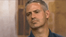 a man with gray hair and a blue shirt is making a funny face .