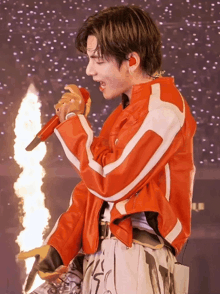 a man in an orange jacket is singing into a red microphone