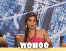 a woman in a pink top is sitting at a table with the word " wohoo " on it