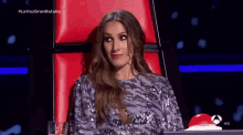 a woman in a sequined dress is sitting in a red chair with the words la voz gran batalla on the bottom