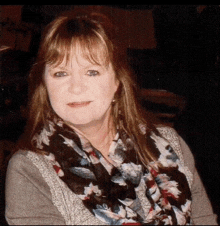 a woman wearing a floral scarf and a sweater looks at the camera