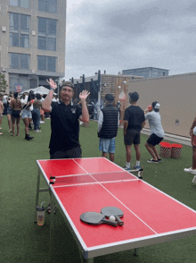 a man stands in front of a red table with ping pong rackets on it