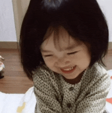 a little girl is sitting on a bed smiling and looking at the camera .