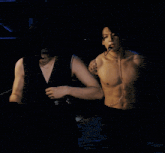 a shirtless man with a microphone around his neck looks at the camera