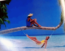 a man sits on a palm tree next to a woman in a hammock on the beach