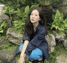 a woman in a blue shirt and blue pants is kneeling on a rock in a garden .