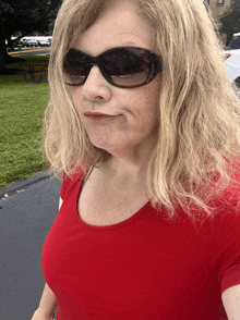 a woman wearing sunglasses and a red shirt is walking down the street