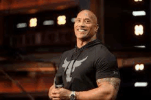 the rock is smiling while standing in front of a microphone in a room .