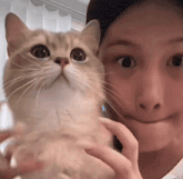 a woman is holding a cat in front of her face and the cat is looking up
