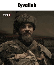 a man with a beard wearing a fur hat with the words trt 1 above him