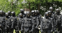 a group of police officers in black uniforms and helmets are standing in a field .