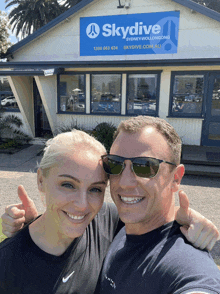 a man and woman are posing for a picture in front of a skydive sign