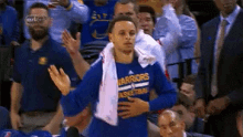 a basketball player wearing a blue shirt with the word warriors on it is standing in front of a crowd .