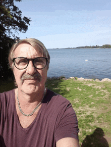 a man with glasses and a mustache is standing in front of a lake