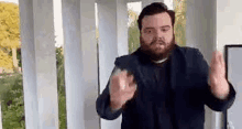 a man with a beard is standing in front of a row of columns and making a funny face .