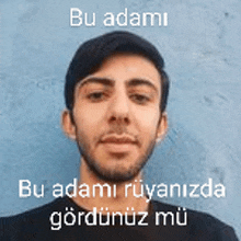 a man with a beard is standing in front of a blue wall and has a foreign language on his face .