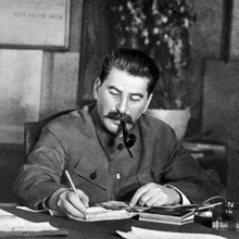 a man with a pipe in his mouth sitting at a desk