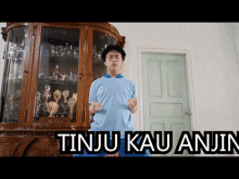 a man in a blue shirt stands in front of a trophy case that says tinju kau anjing on it