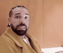 a man with a beard and braids is wearing a yellow jacket and earrings .