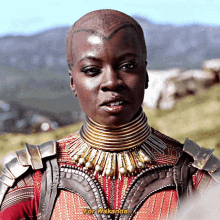 a woman with a shaved head is wearing a necklace and armor and says " for wakanda "