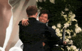 two men hugging each other in front of flowers