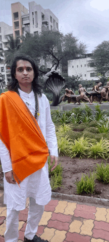 a man wearing a white shirt and an orange scarf is standing in front of a statue