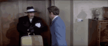 two men are standing next to each other in a room and one has a briefcase