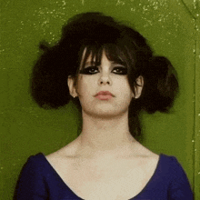 a woman with a bun in her hair is wearing a blue dress and looking at the camera .