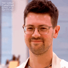 a man with glasses and a beard is smiling in front of a sign for the great canadian baking show