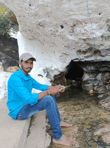 a man in a blue shirt is sitting next to a cave