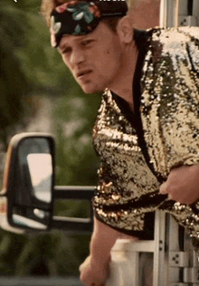 a man wearing a sequined shirt and a headband is standing in front of a truck