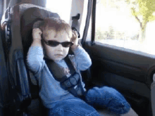 a little boy wearing sunglasses and a seat belt is sitting in a car seat